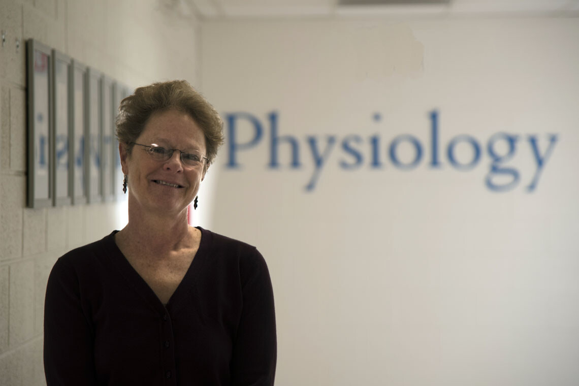 Photo of Professor Pat Brubaker with a sign that says Physiology behind her