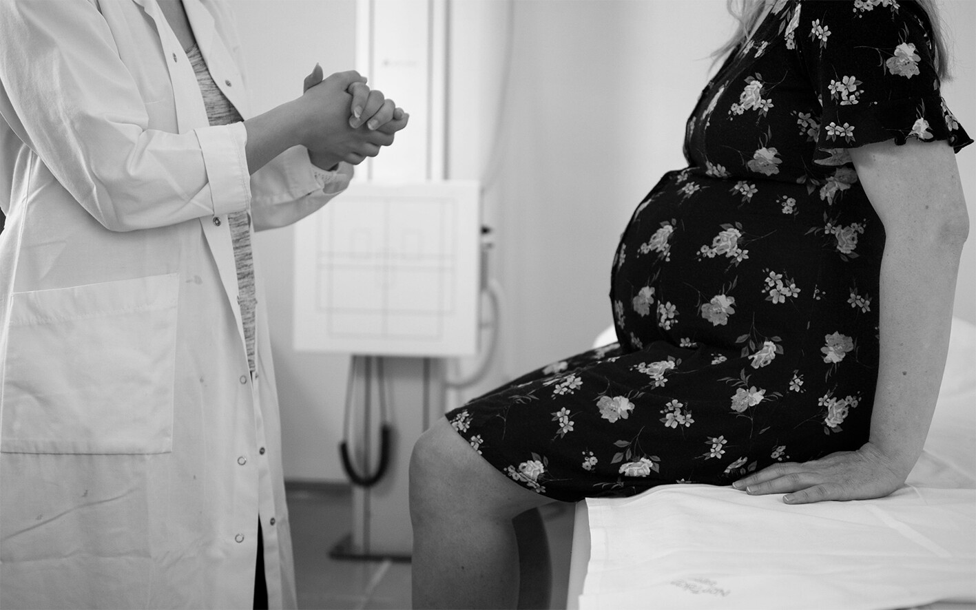 A pregnant person speaking with a doctor. We see both of their torsos, not their heads or faces.