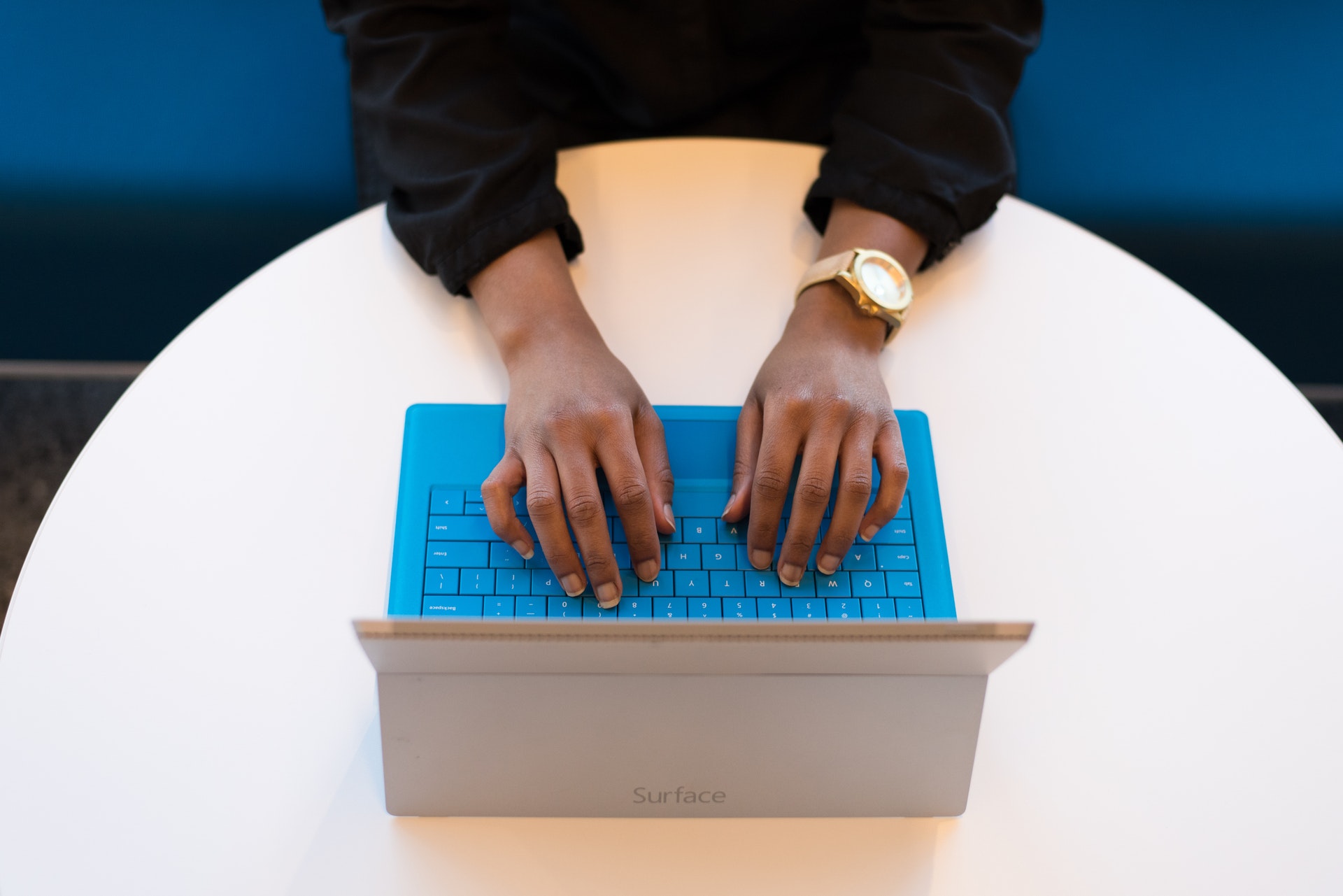 Photo of a Black person's hands typing on a laptop with a blue keyboard